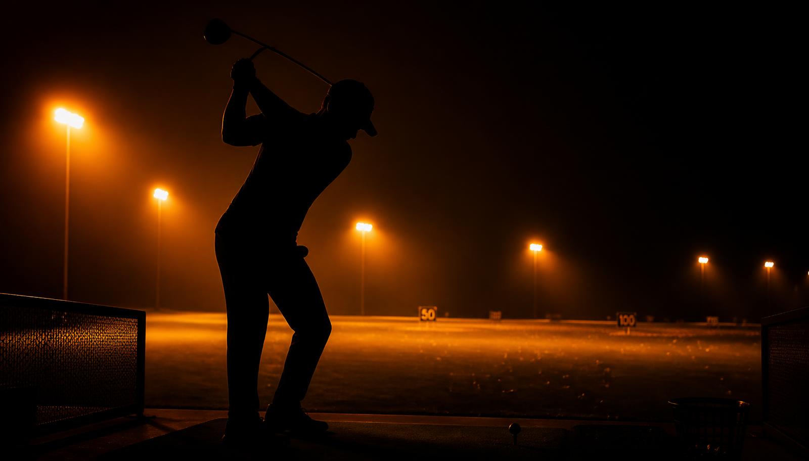 Golfer silhouette at the top of the backswing under range lights